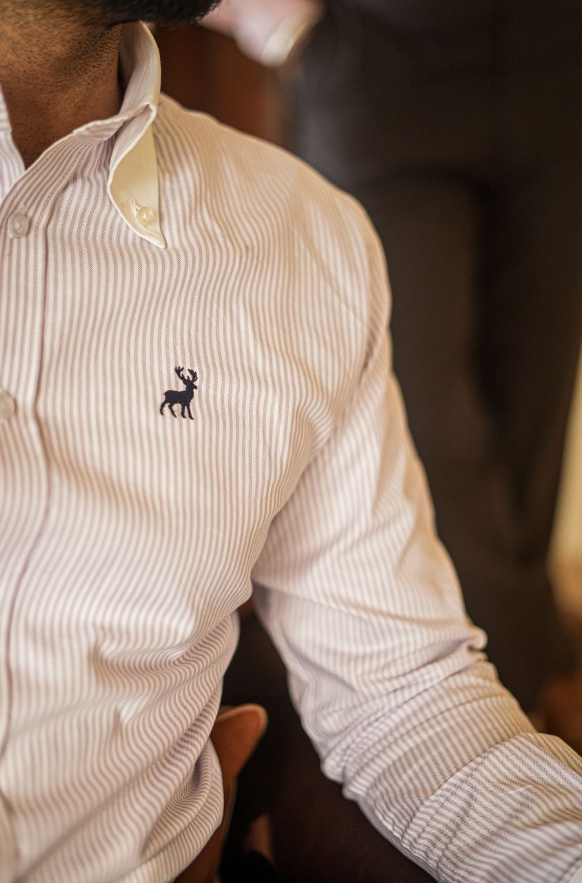Close-up of a person wearing a light-colored Oxford shirt with a small logo of luxento on the chest.