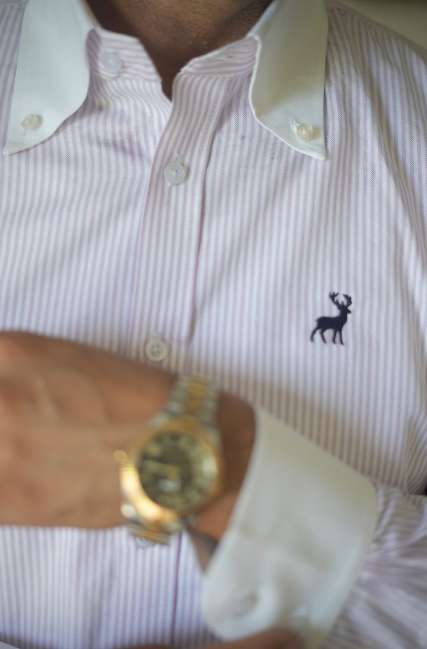 Close-up of a person wearing a striped shirt with a logo and a gold watch.