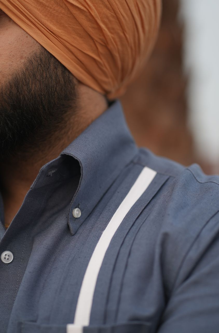 Close-up of a person wearing a blue shirt with a white stripe and an orange turban.