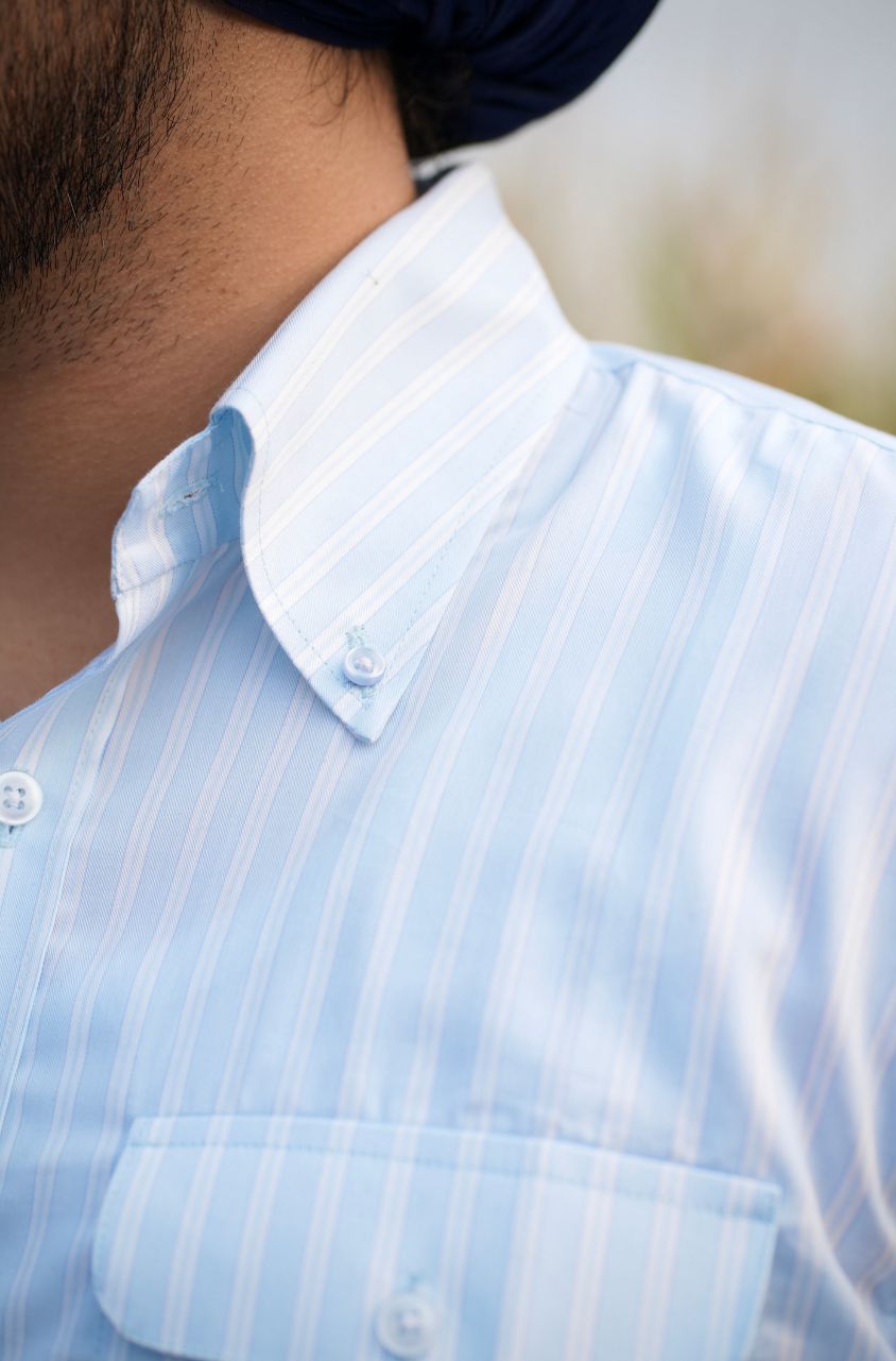 Close-up of a person wearing a light blue striped shirt with a blurred background