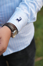 Close-up of a person wearing a light blue shirt with rolled-up sleeves and a watch, with a blurred green background.