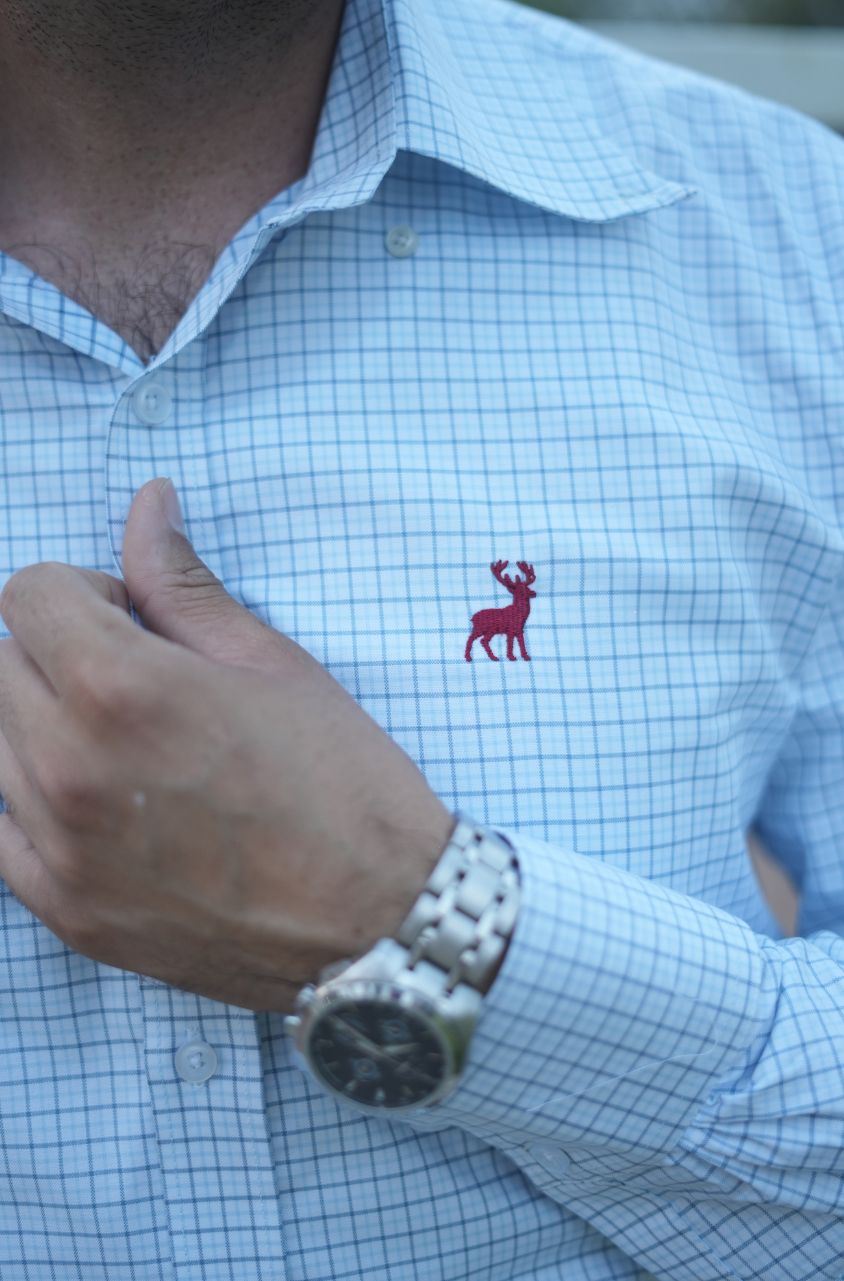 Close-up of a person wearing a blue checkered shirt with a red deer emblem and a silver watch.