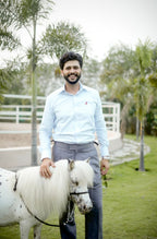 Man standing next to a small white horse in an outdoor setting with greenery.