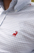Close-up of a checkered shirt with a red embroidered deer logo on a blurred background