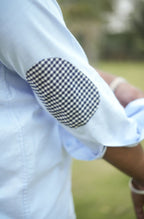 Close-up of a person wearing a light blue shirt with a checkered elbow patch.