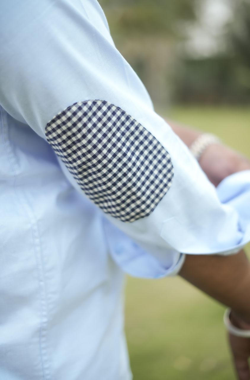 Close-up of a person wearing a light blue shirt with a checkered elbow patch.