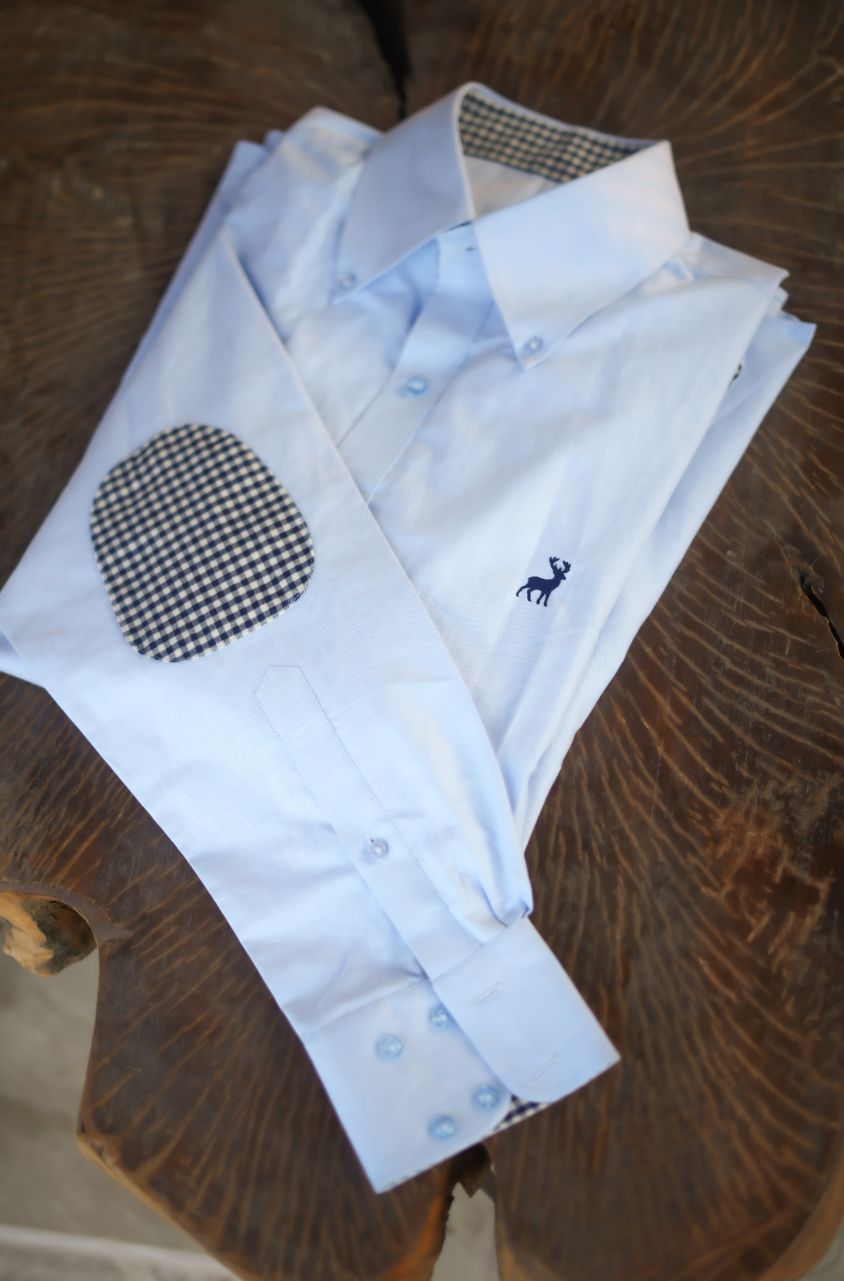 Folded white dress shirts with embroidered designs on a wooden surface by luxento