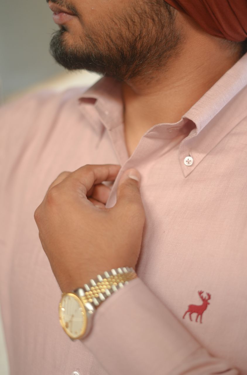 Close-up of a person wearing a pink shirt with a gold watch and red emblem.