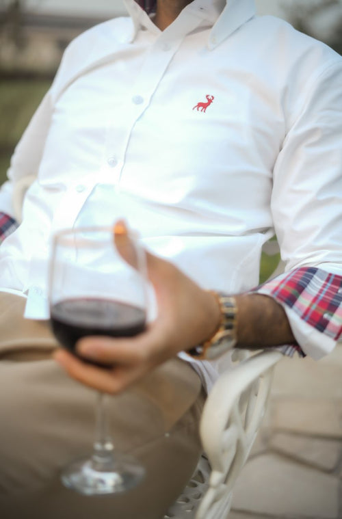 Person holding a glass of red wine, wearing a white shirt with a logo.