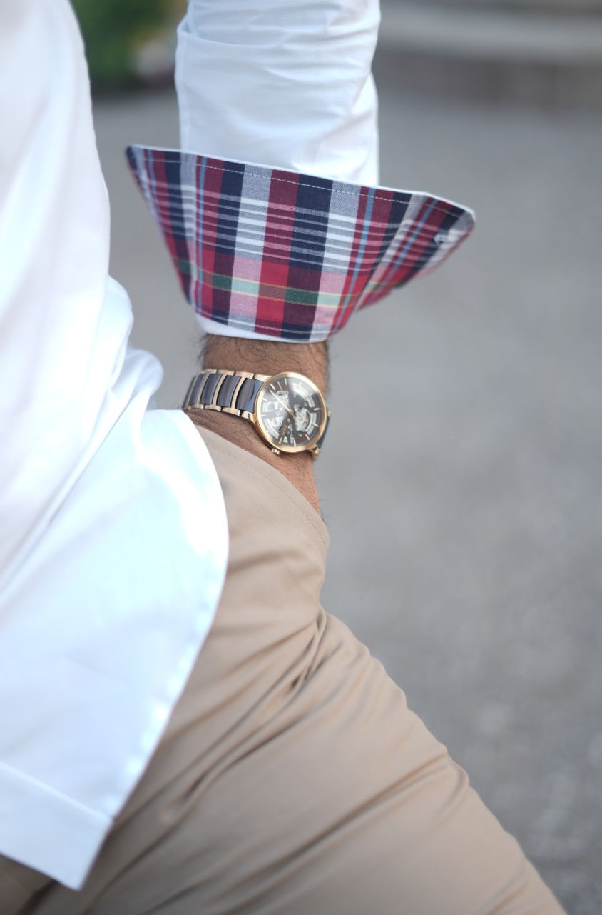 Close-up of a person wearing a plaid cuff, white shirt, beige pants, and gold watch.
